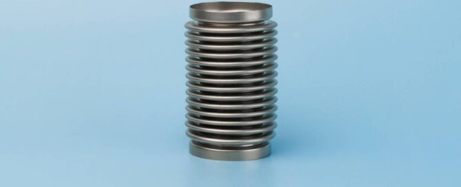A silver metal bellows sits on a completely blue surface and in front of a background with the same color.